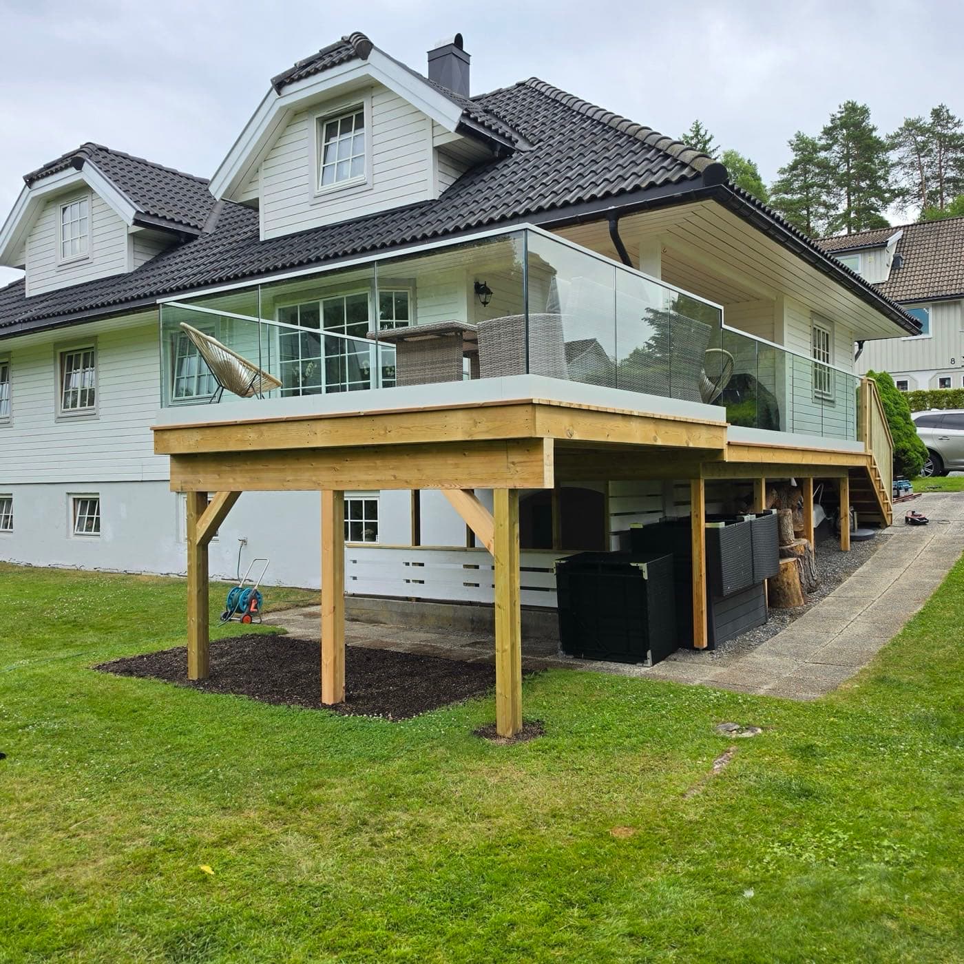 Opphøyd terrasse på søyler med glassrekkverk bygget inntil bolig, Ås